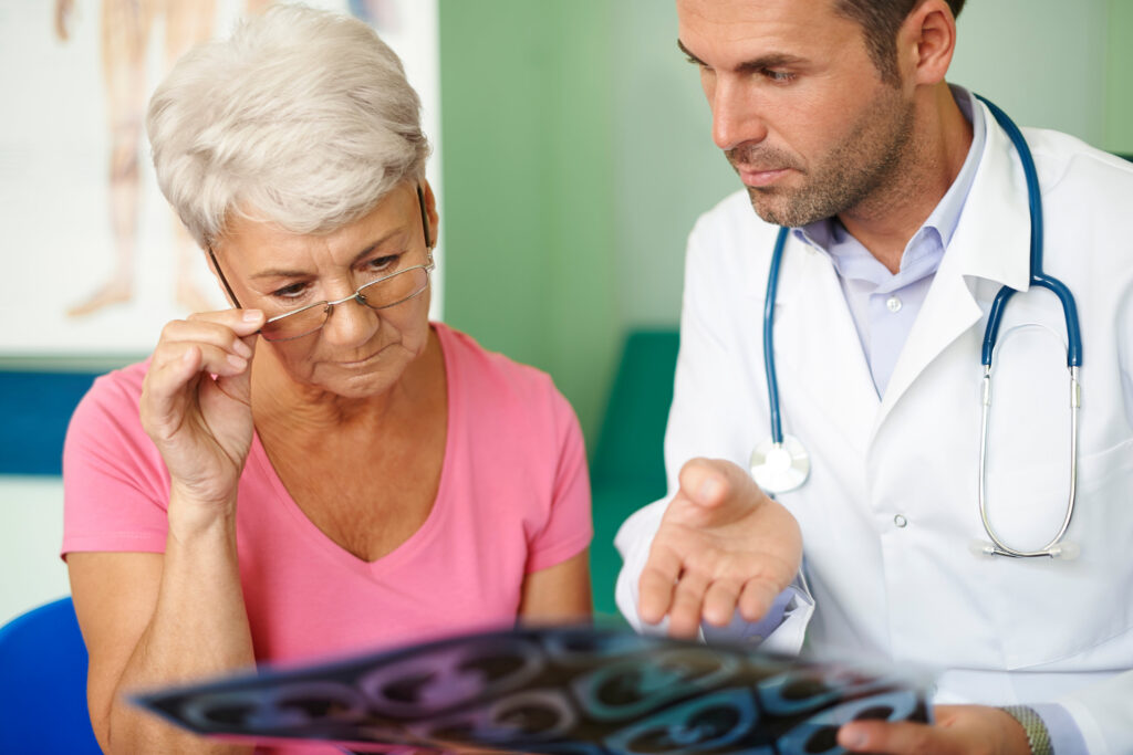 A doctor explains migraine management to an older woman during a consultation in a healthcare environment.