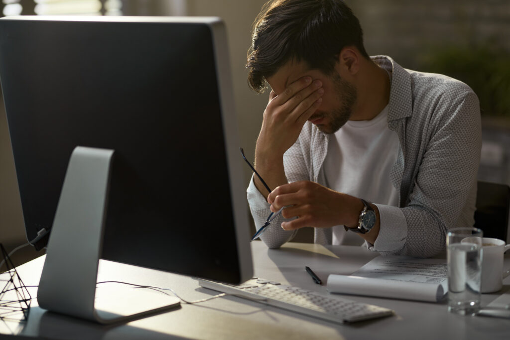 A man sits at a desk, resting his head in his hands, conveying a sense of stress or frustration.