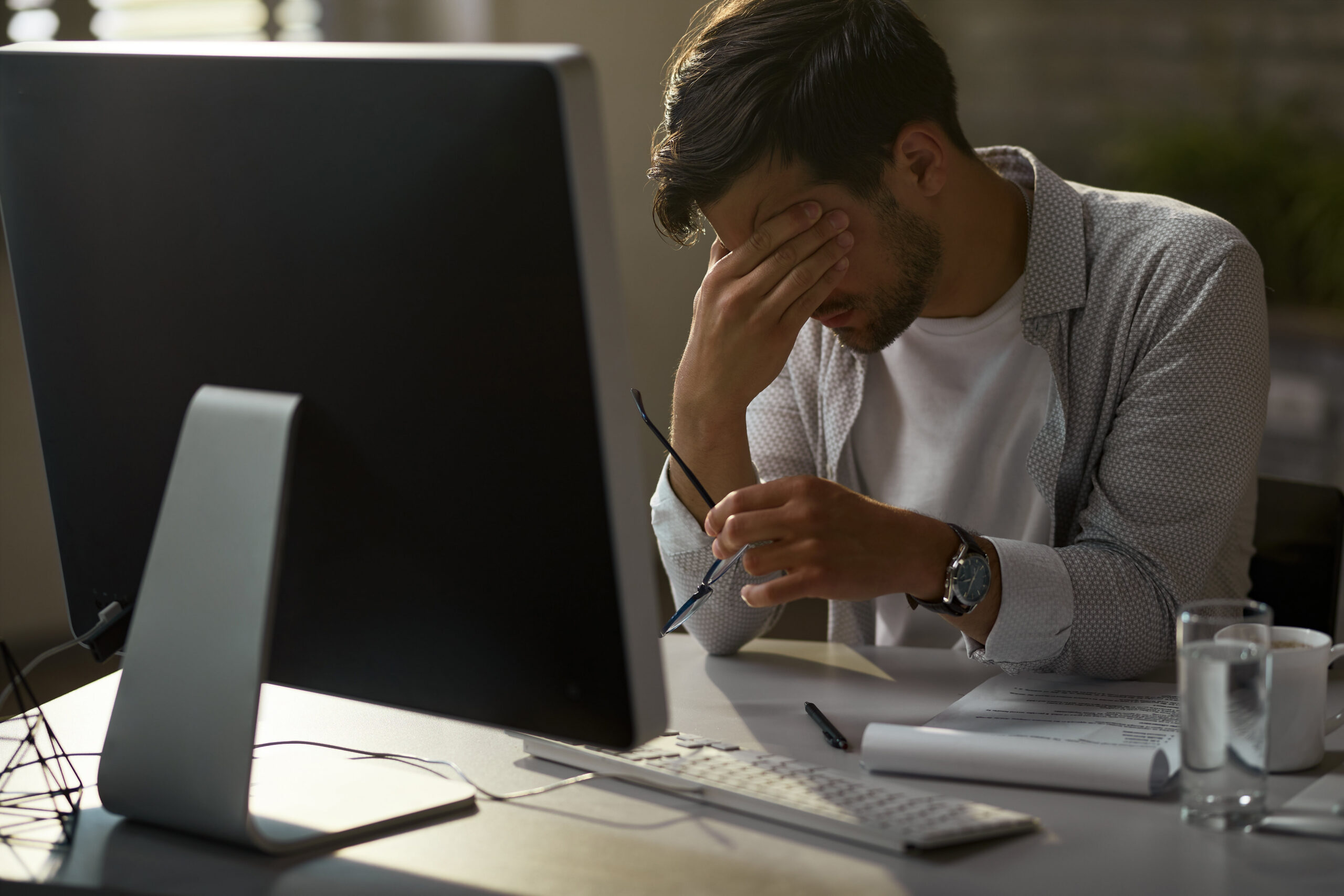 A man sits at a desk, resting his head in his hands, conveying a sense of stress or frustration.