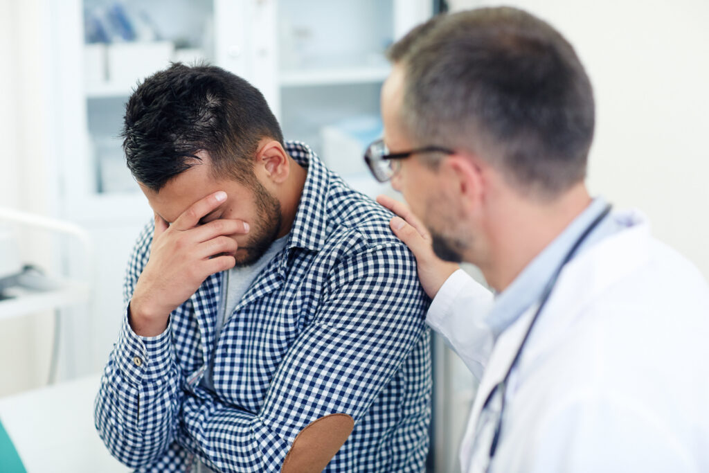 A man sitting in an office holds his head, indicating discomfort, possibly due to a migraine.