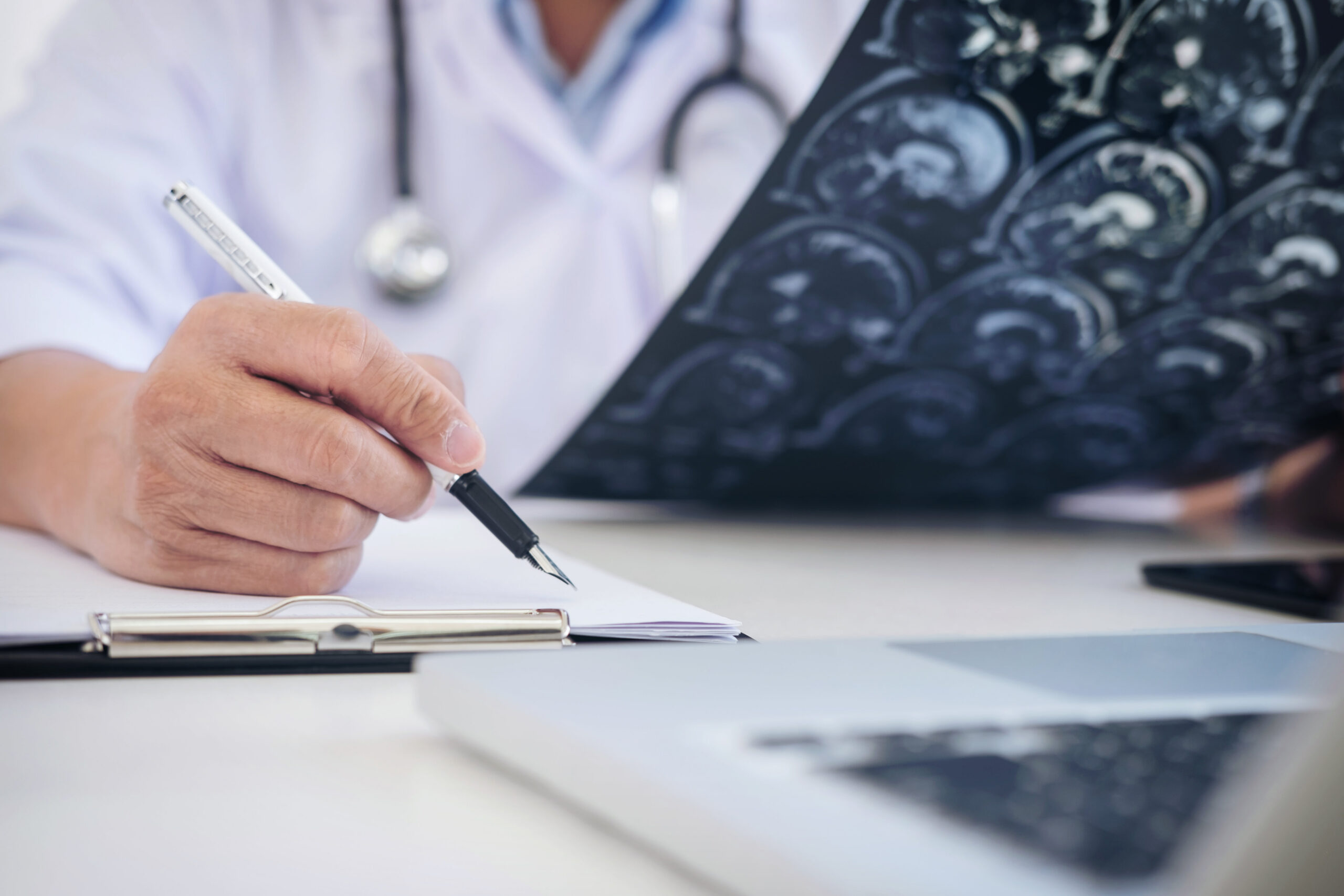 A doctor writes notes on paper while examining an MRI scan for patient evaluation.